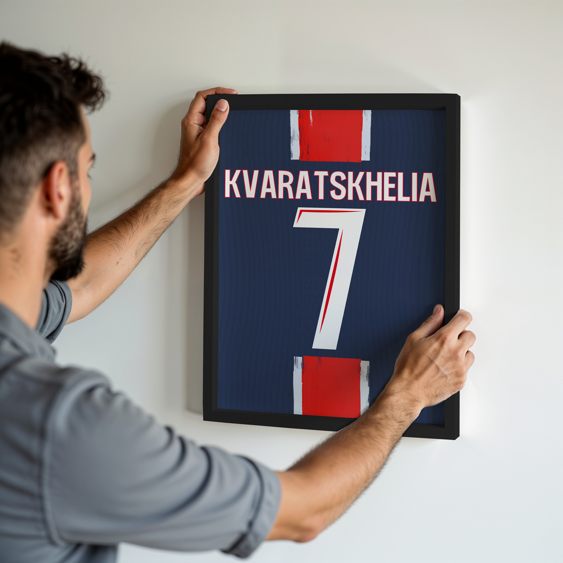 Un homme accroche un cadre personnalisé de football au mur, représentant le maillot bleu de Kvaratskhelia avec le numéro 7, inspiré du PSG